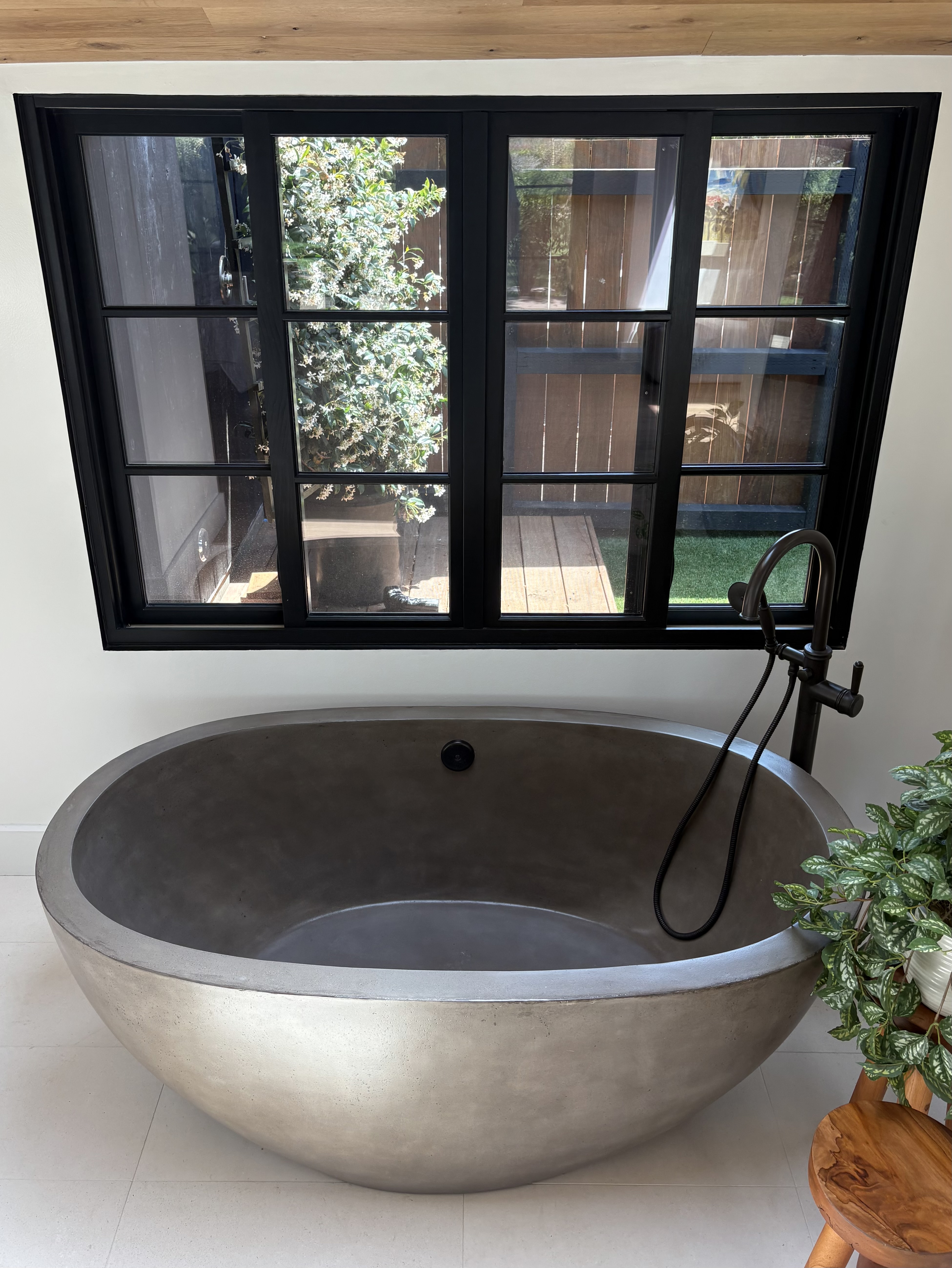 Freestanding concrete soaking tub with matte black wall-mount faucet and large black-framed window